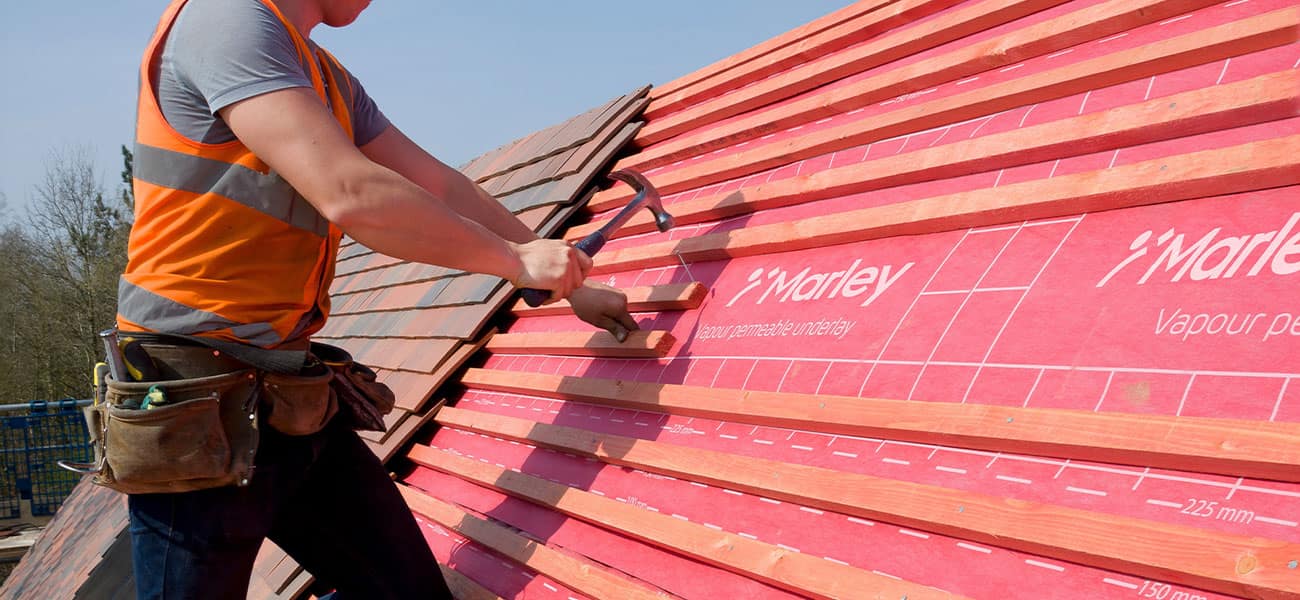 A roofer installing a complete Marley roof system with clay roof tiles